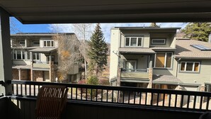 Een balkon met een houten stoel, met uitzicht op een rij herenhuisen met stenen details en een helder zicht op de omliggende buurt.