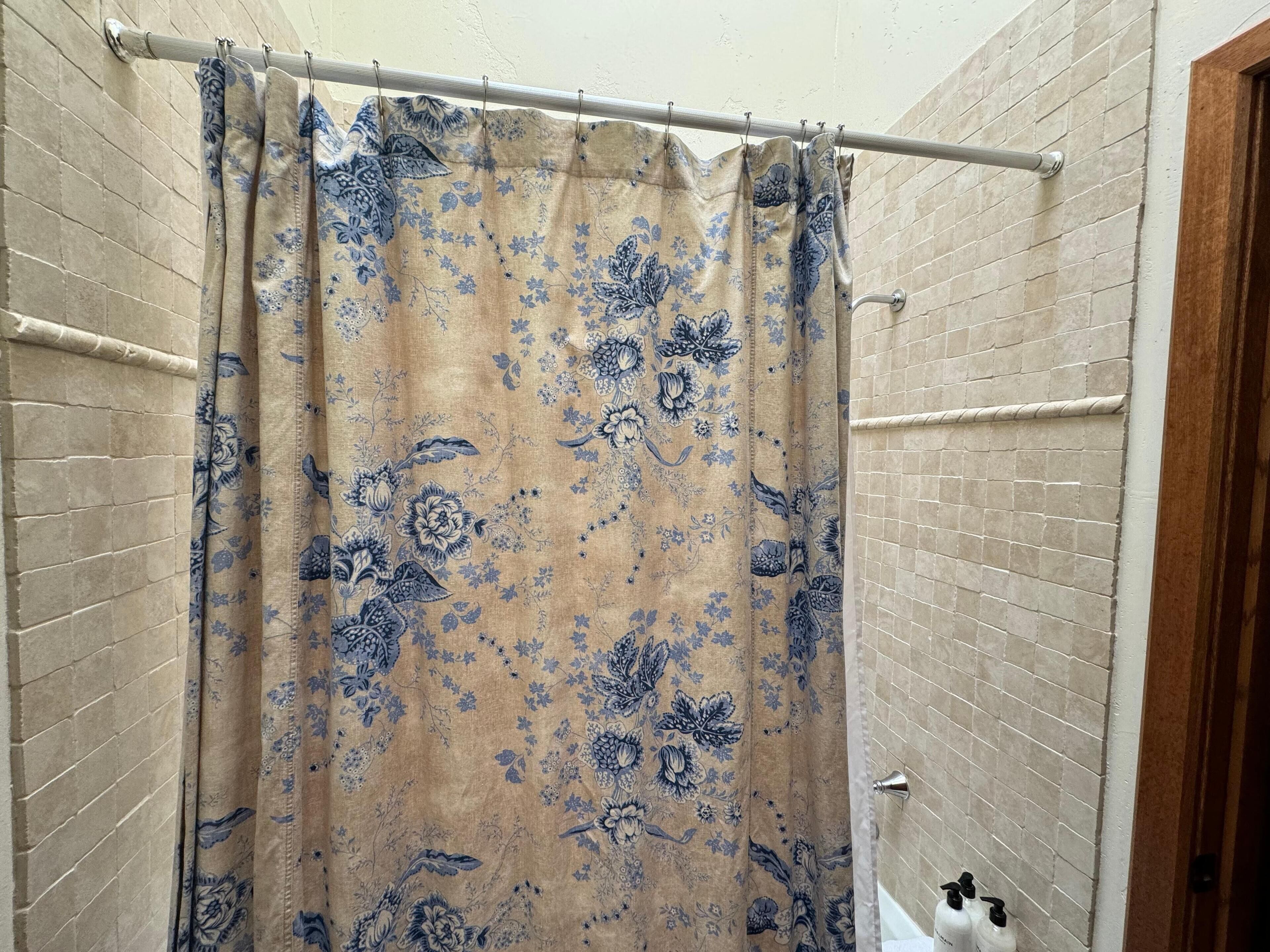 Une salle de bain avec un mur en briques de couleur beige, un rideau de douche à motifs floraux et une tringle à rideau en métal.