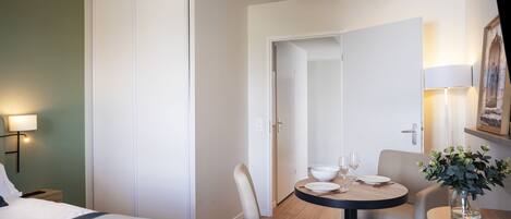 Habitación de hotel con cama, una mesa redonda con sillas, un jarrón con flores y un cuadro en la pared.