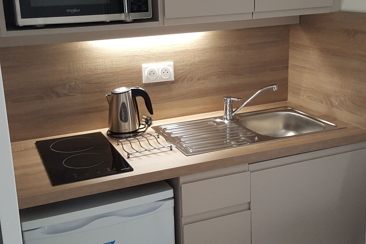 A compact kitchen with a microwave, kettle, induction cooktop, sink, and dishwasher.