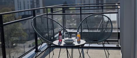 A balcony with two chairs, a table, and a bottle of orange juice.