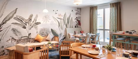 A dining area with a high ceiling, a mural of tropical plants, and a view of the outside.