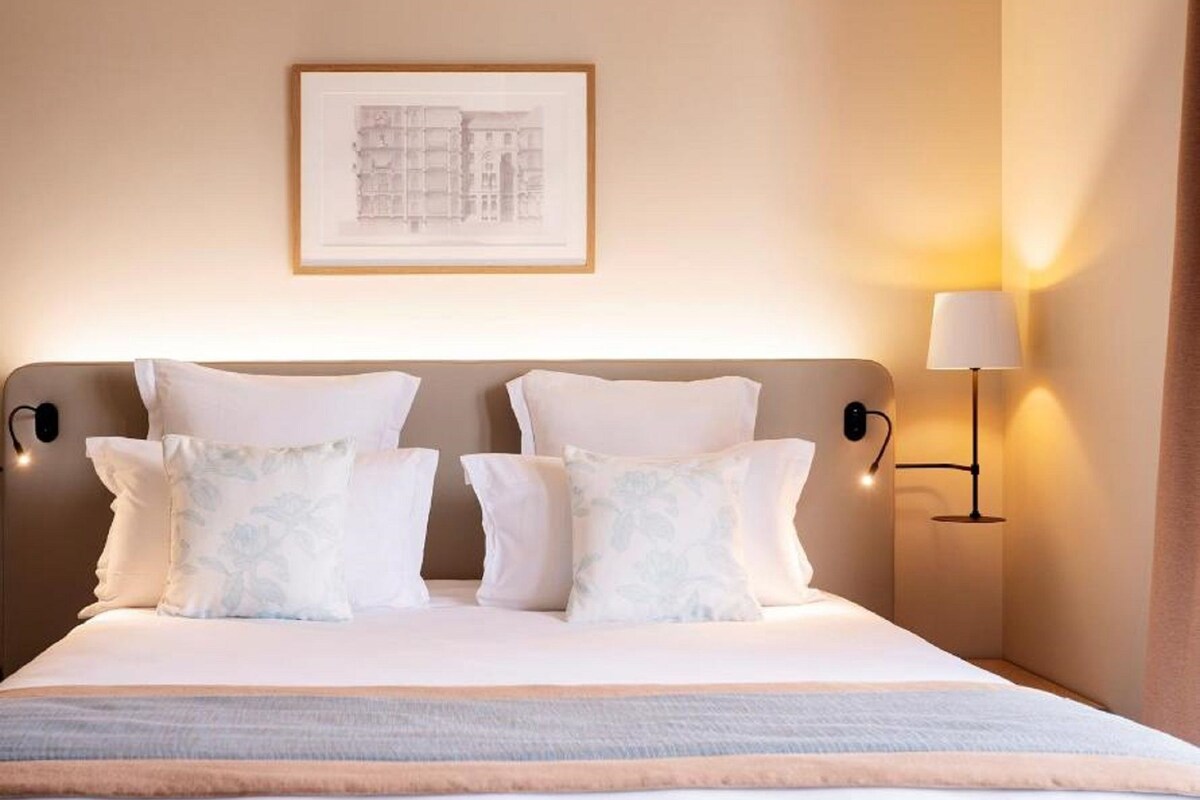 A hotel room with a bed, pillows, a framed picture on the wall, and a bedside lamp.