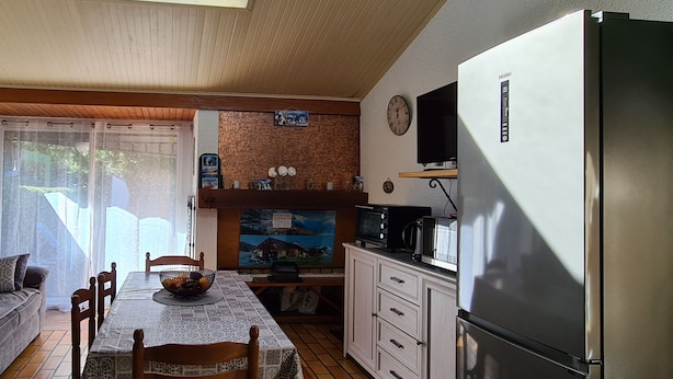 A cozy kitchen with a dining table, wooden chairs, a refrigerator, and a television.