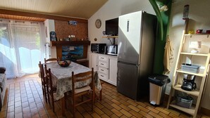 A compact kitchen with a refrigerator, microwave, and coffee maker. There is a dining table with chairs and a window with curtains.