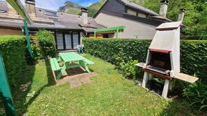A backyard with a green picnic table, a barbecue grill, and a house with a sloped roof.