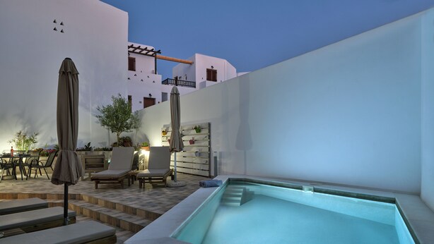 Un área de piscina en la azotea con sillones, un jacuzzi y una pérgola.