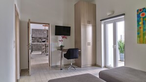 Una habitación moderna con dos camas, un televisor, un escritorio con silla, un armario grande y vista a la cocina por una puerta abierta.