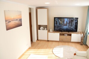 Un salon moderne avec un téléviseur à écran plat, des meubles en bois, un tapis rond et un tableau accroché au mur.