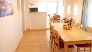 Un comedor con una mesa y sillas de madera, un frutero sobre la mesa y una cocina al fondo.