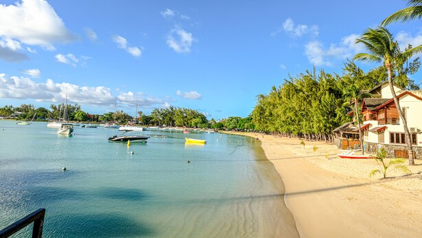 Une plage avec une eau turquoise et limpide, des bateaux et un bâtiment doté d’un balcon donnant sur la mer.