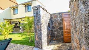 Un mur de pierre avec une porte en bois, une cour gazonnée et une terrasse avec une chaise.