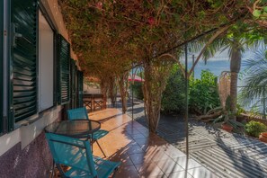 A covered patio with a table and chairs, a view of the sea, and a pergola with climbing plants. - Villa Flora (Calheta)