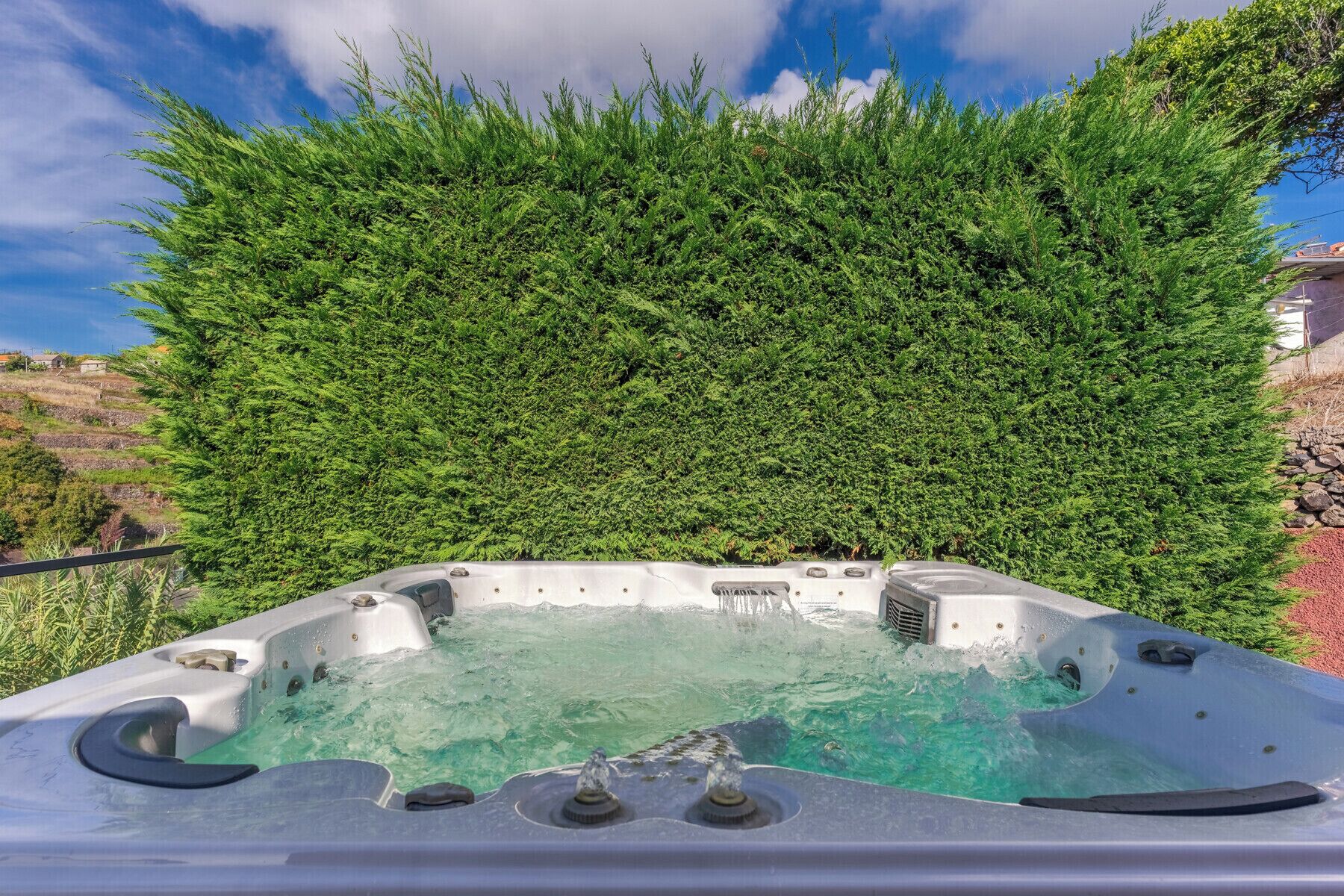 Ein Whirlpool mit freiem Blick auf die Umgebung, darunter ein dichter Grünstreifen und ein Kiesweg.