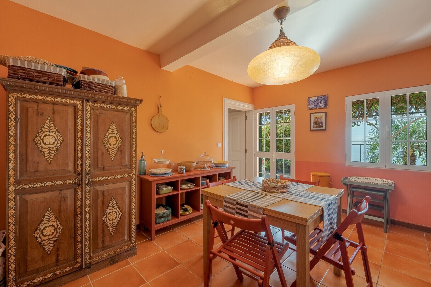 A dining area with a wooden table and chairs, a cabinet with decorative carvings, and a hanging light fixture.