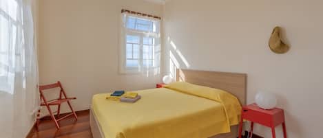 A bedroom with a wooden bed, a red nightstand, a white lamp, and a window with curtains.