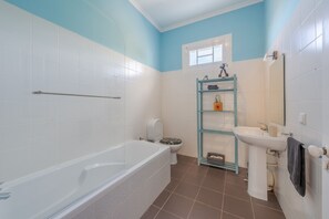 A bathroom with a bathtub, toilet, and sink, featuring white and blue walls and brown tiles. - Villa Flora (Calheta)