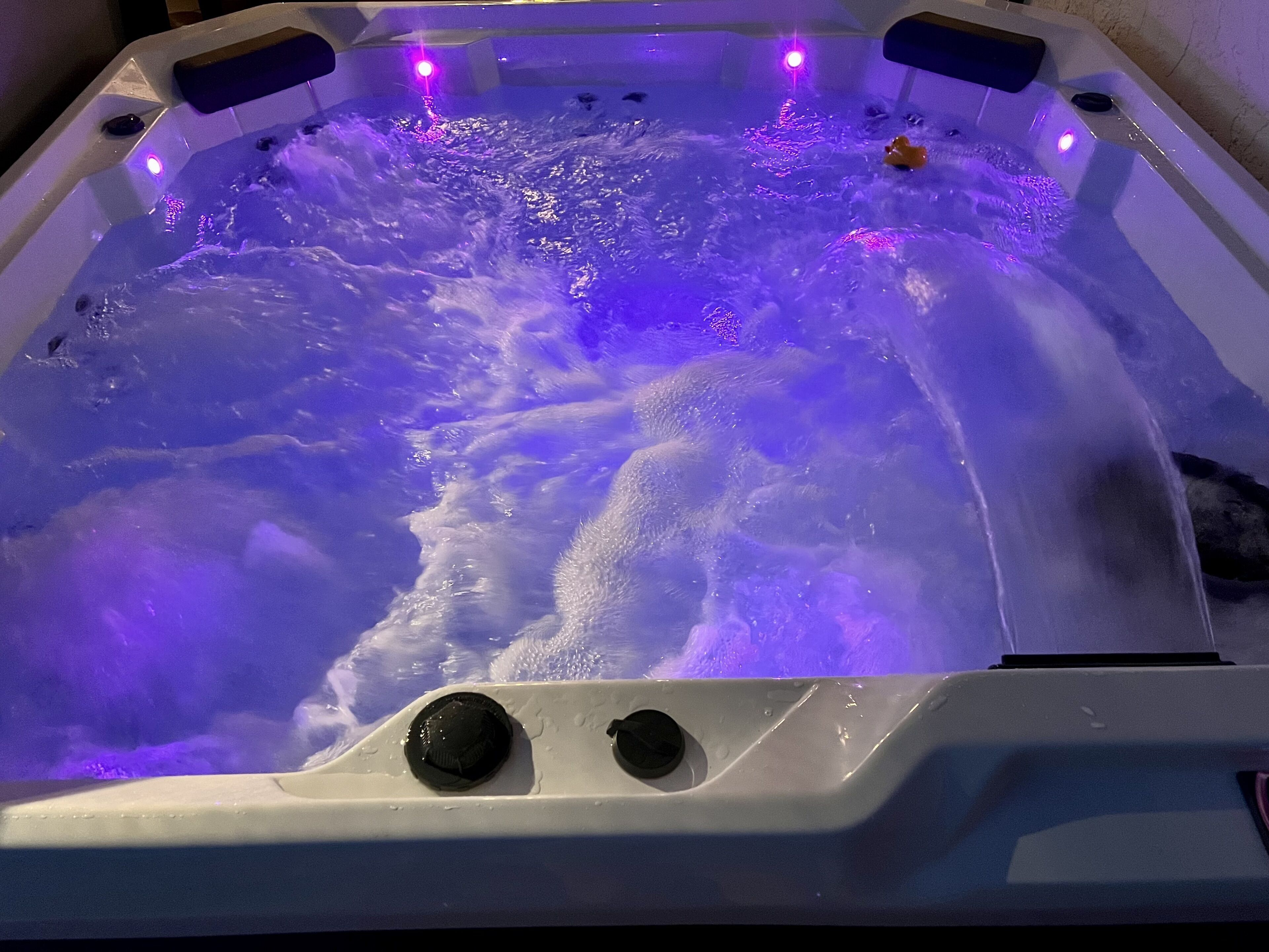 Ein Whirlpool mit violetter Beleuchtung, zwei Bedienelementen und einem Quietscheentchen.