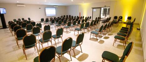 A conference room with rows of green chairs and a projection screen.