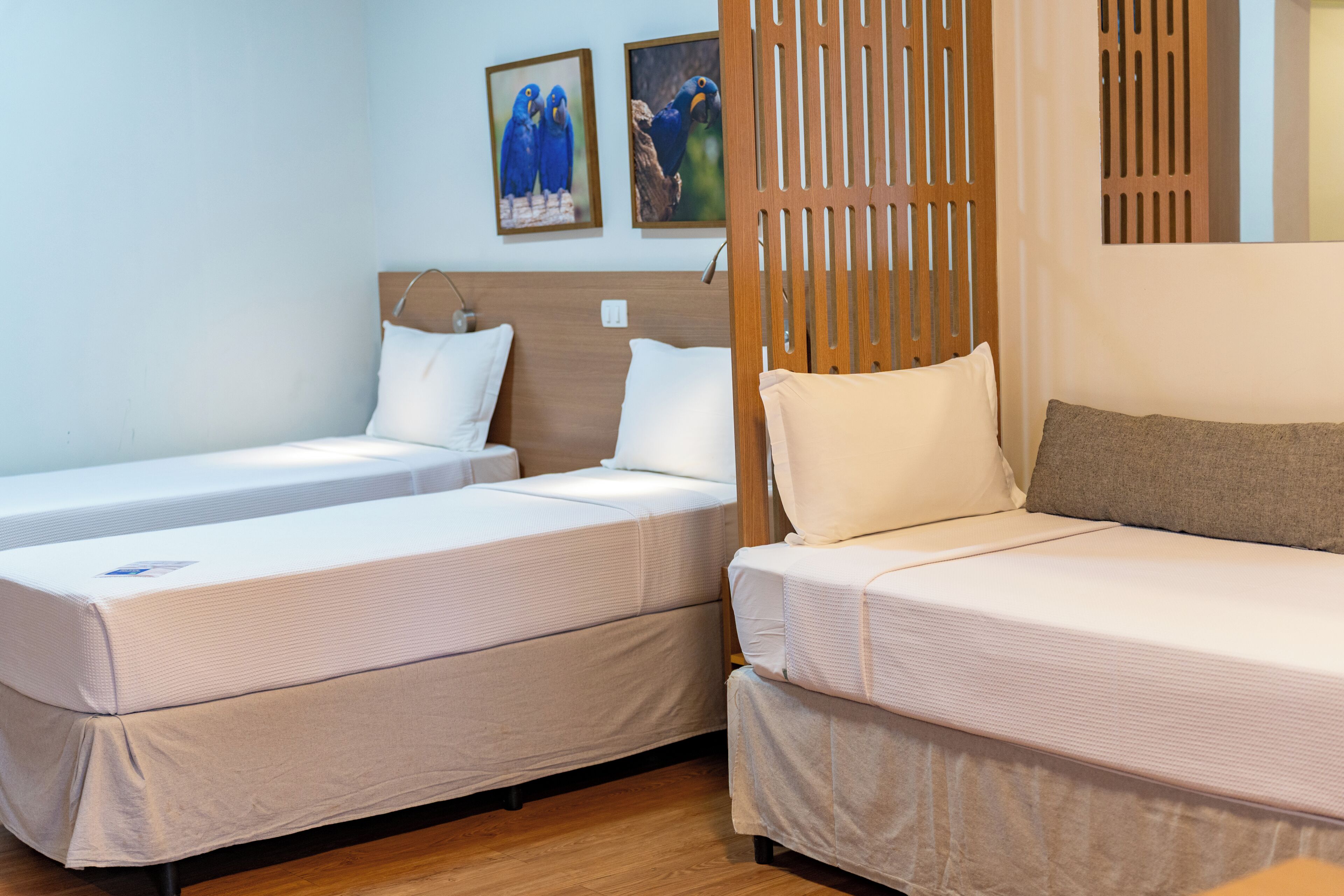 A hotel room with two single beds, a sofa, wooden headboard, and two framed pictures on the wall.