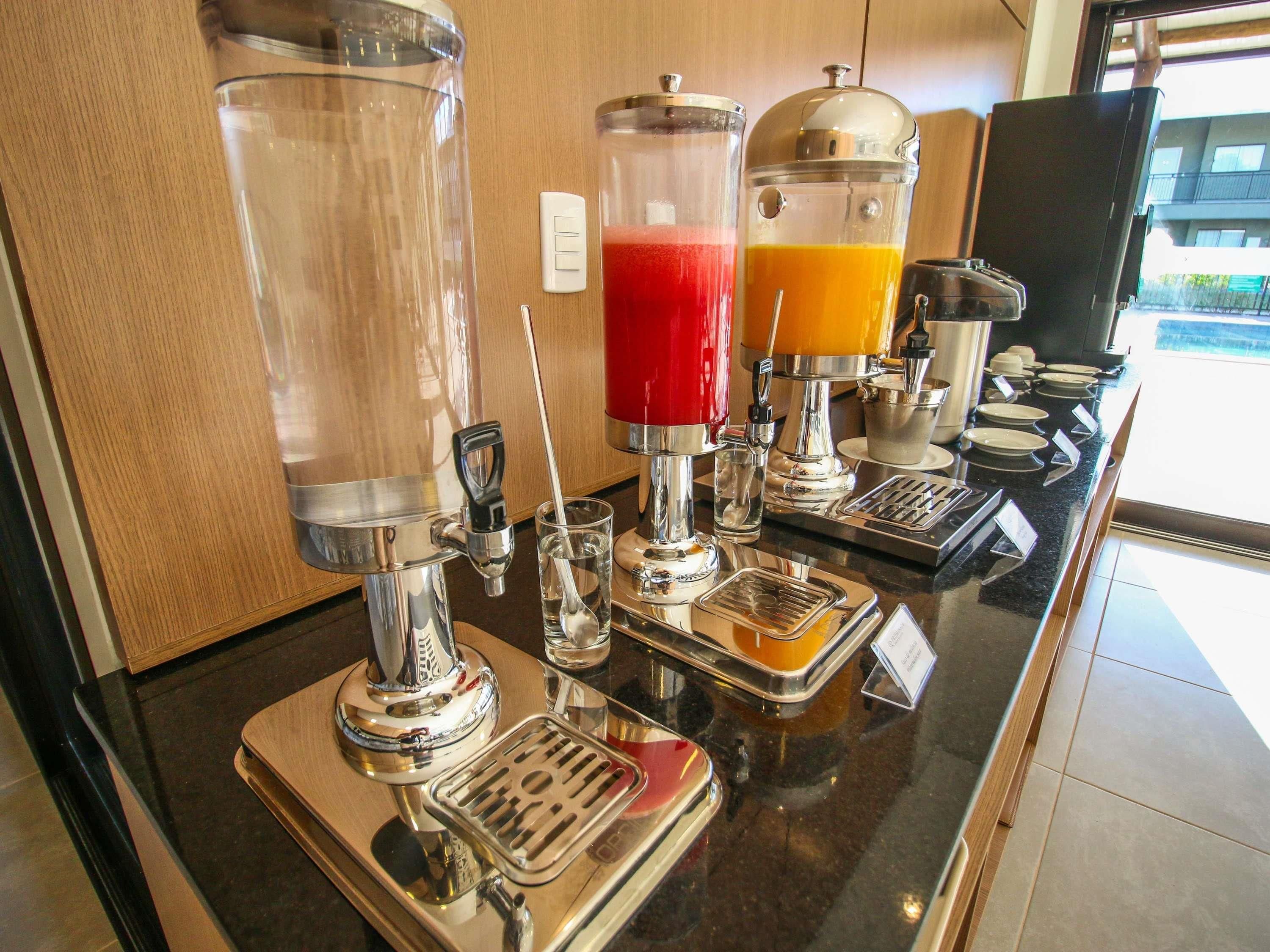 Zona de bar con una máquina de café, dispensador de zumo y un vaso de agua.