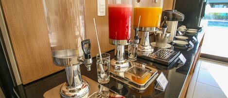 Zona de bar con una máquina de café, dispensador de zumo y un vaso de agua.