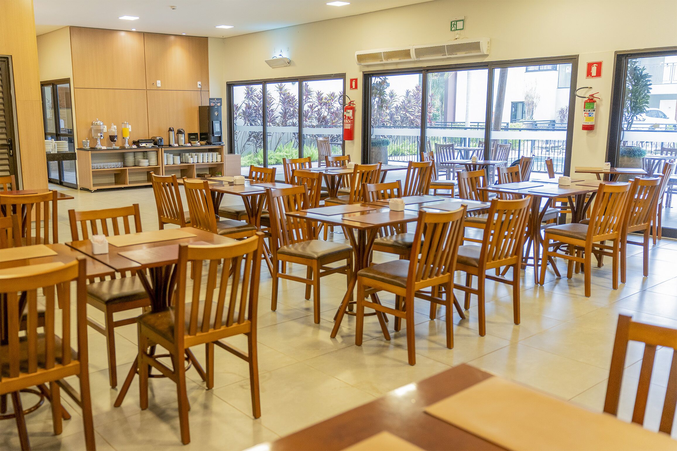 Un vaste espace dédié à la restauration, avec de nombreuses tables et chaises en bois, un buffet proposant une variété de plats et de boissons, et de grandes fenêtres offrant une vue sur l’extérieur.