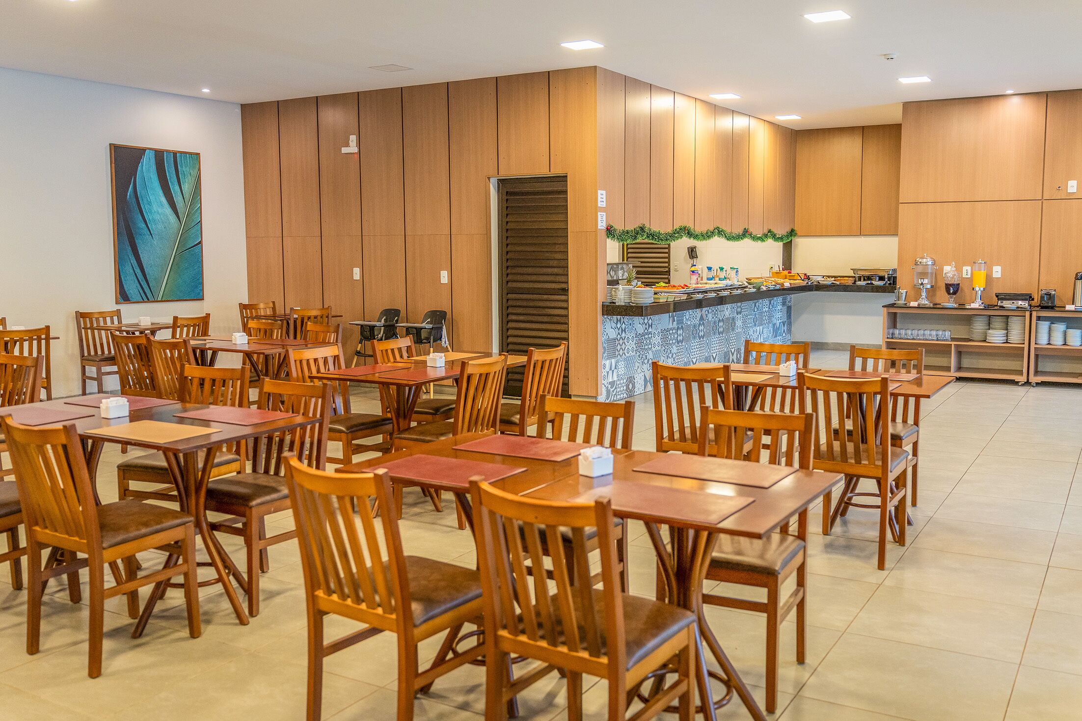 A spacious dining area with wooden tables and chairs, a kitchen area with a bar, and a large painting on the wall.