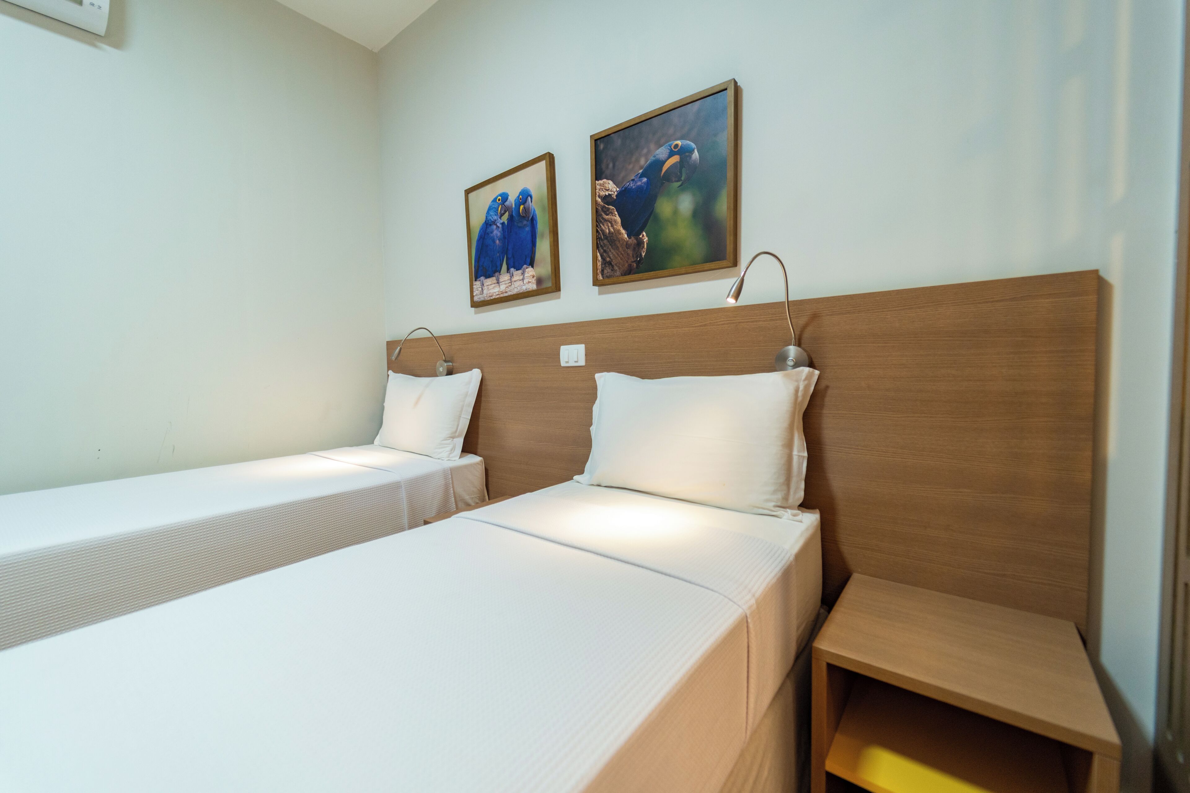 A hotel room with two single beds, a wooden headboard, and two framed pictures on the wall.
