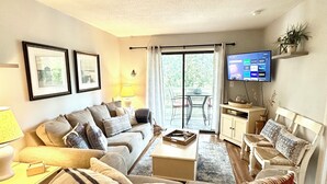 Un salon comprenant un canapé, un fauteuil, une table basse et un téléviseur fixé au mur.