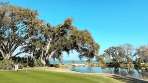Un parcours de golf avec un étang, des arbres et un ciel bleu dégagé.