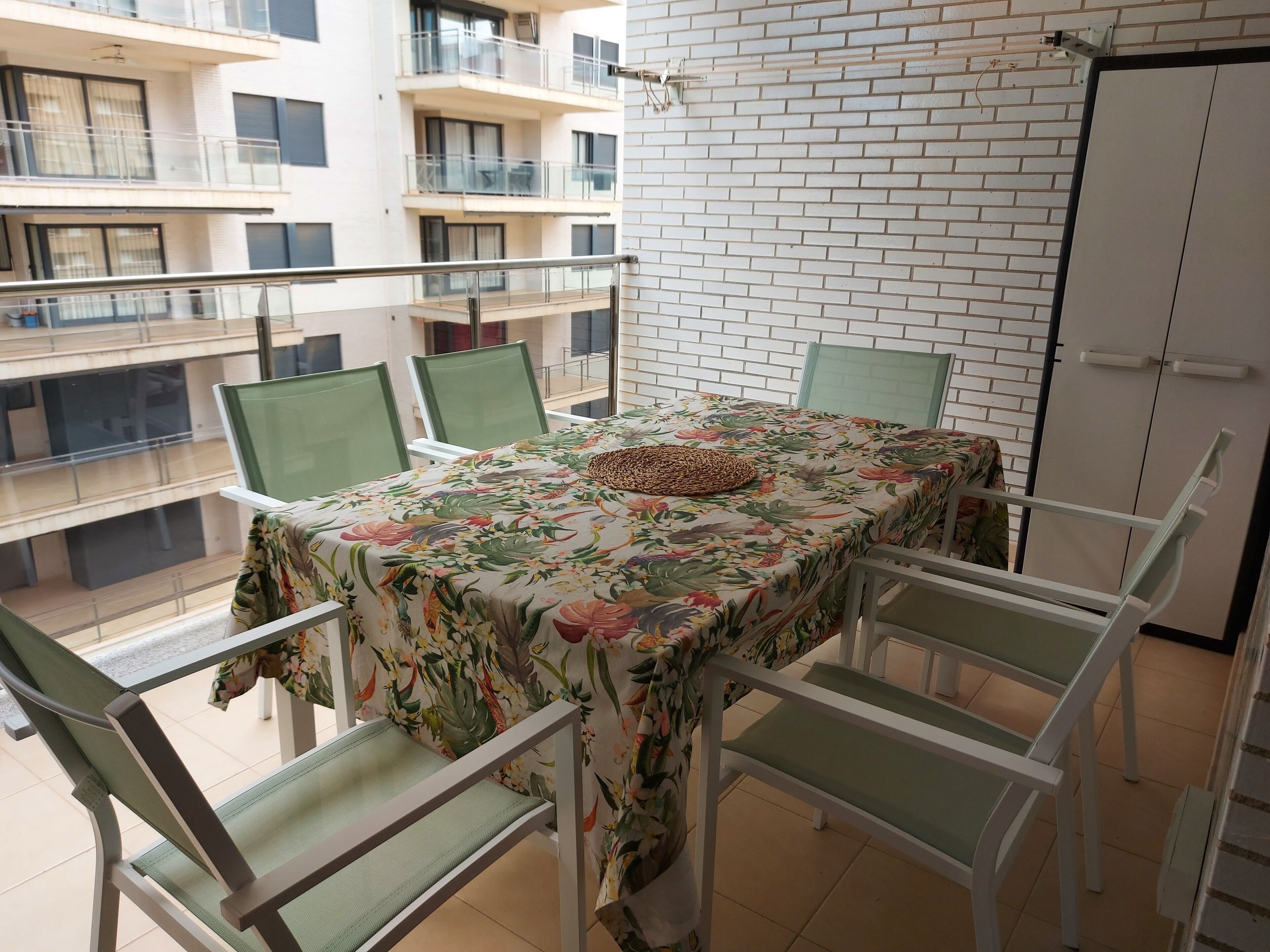 Un balcon avec une table et des chaises, une nappe à motifs et une vue sur les bâtiments voisins.
