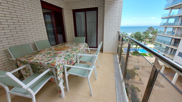 A balcony with a dining table and chairs, a view of the sea, and a building with balconies. - MARINA BEACH APARTMENT (Oropesa del Mar)
