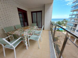 A balcony with a dining table and chairs, a view of the sea, and a building with balconies. - MARINA BEACH APARTMENT (Oropesa del Mar)