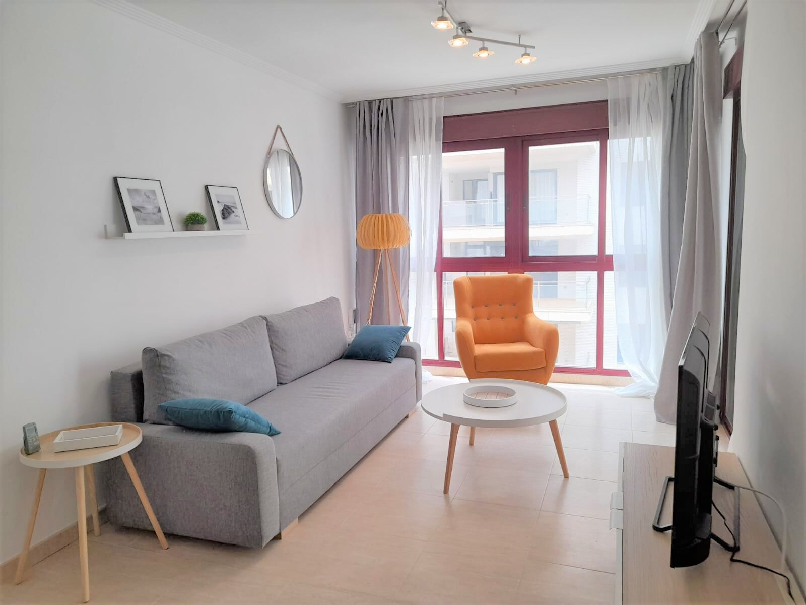 A modern living room with a grey sofa, an orange armchair, a small round coffee table, and a TV on a stand.
