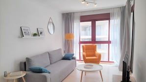 A modern living room with a grey sofa, an orange armchair, a small round coffee table, and a TV on a stand. - MARINA BEACH APARTMENT (Oropesa del Mar)