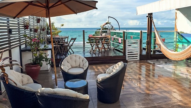 A rooftop terrace with wicker furniture, a large umbrella, and a view of the ocean. - Pousada Tropical Maragogi (Maragogi)