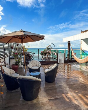 A rooftop terrace with wicker furniture, a large umbrella, and a view of the ocean. - Pousada Tropical Maragogi (Maragogi)