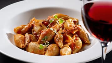 Un plato de pasta con salsa roja y una copa de vino tinto.