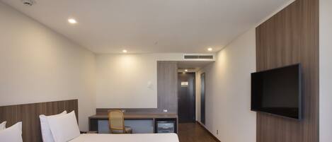 A hotel room with a bed, desk, chair, TV, and a small kitchenette.