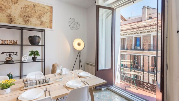 Un coin repas avec une table dressée pour quatre personnes, une carte du monde accrochée au mur, un lampadaire et une vue sur le paysage urbain, visible à travers la porte-fenêtre du balcon.
