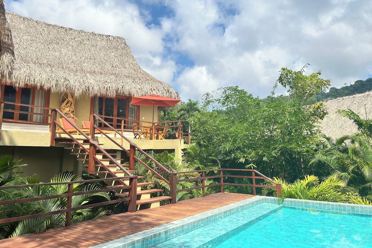 A resort with a pool, wooden deck, and a thatched-roof building.