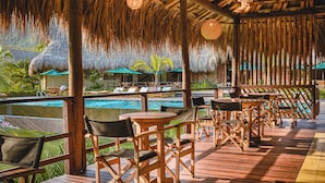 A wooden deck with lounge chairs and umbrellas, a pool, and a thatched roof structure. - Senda Watapuy (Santa Marta)
