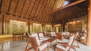 A spacious lounge with wooden furniture and a patterned floor, featuring a thatched roof and wall-mounted displays. - Senda Watapuy (Santa Marta)