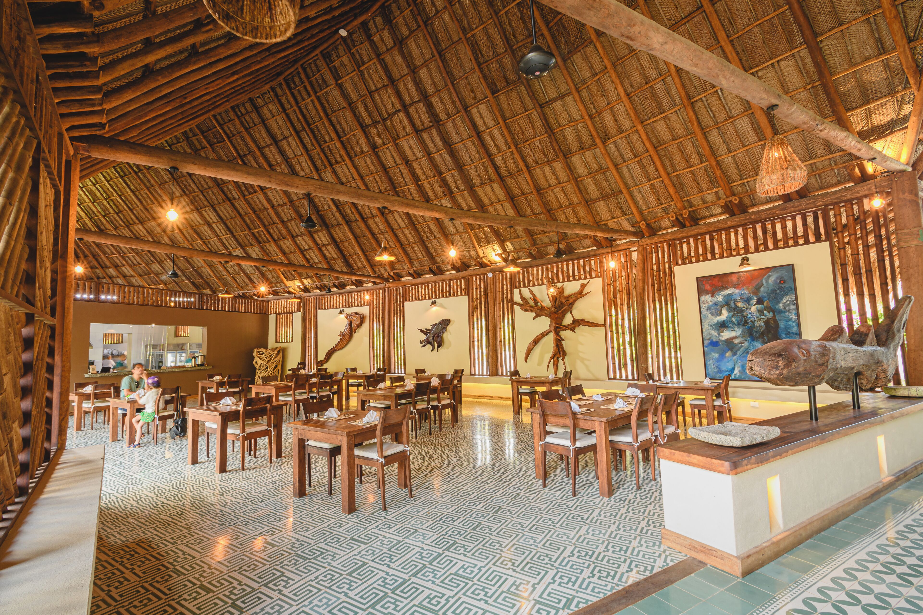 Un restaurante espacioso con mobiliario de madera, techo de paja y decoración mural.