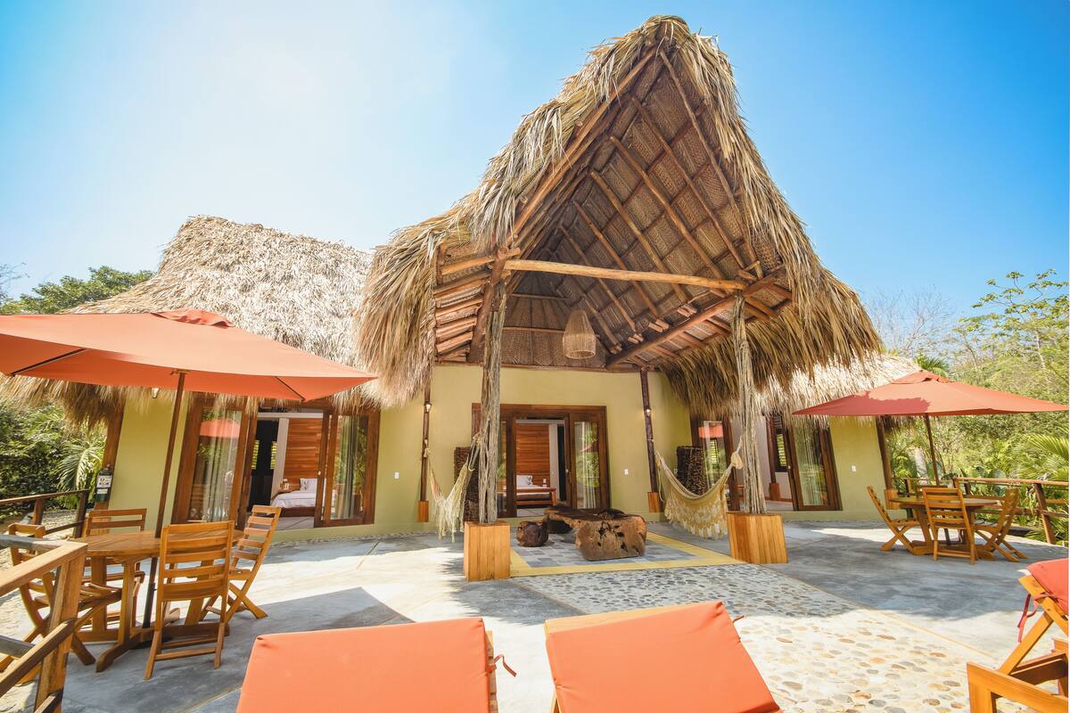 A thatched-roof building with wooden furniture and umbrellas.