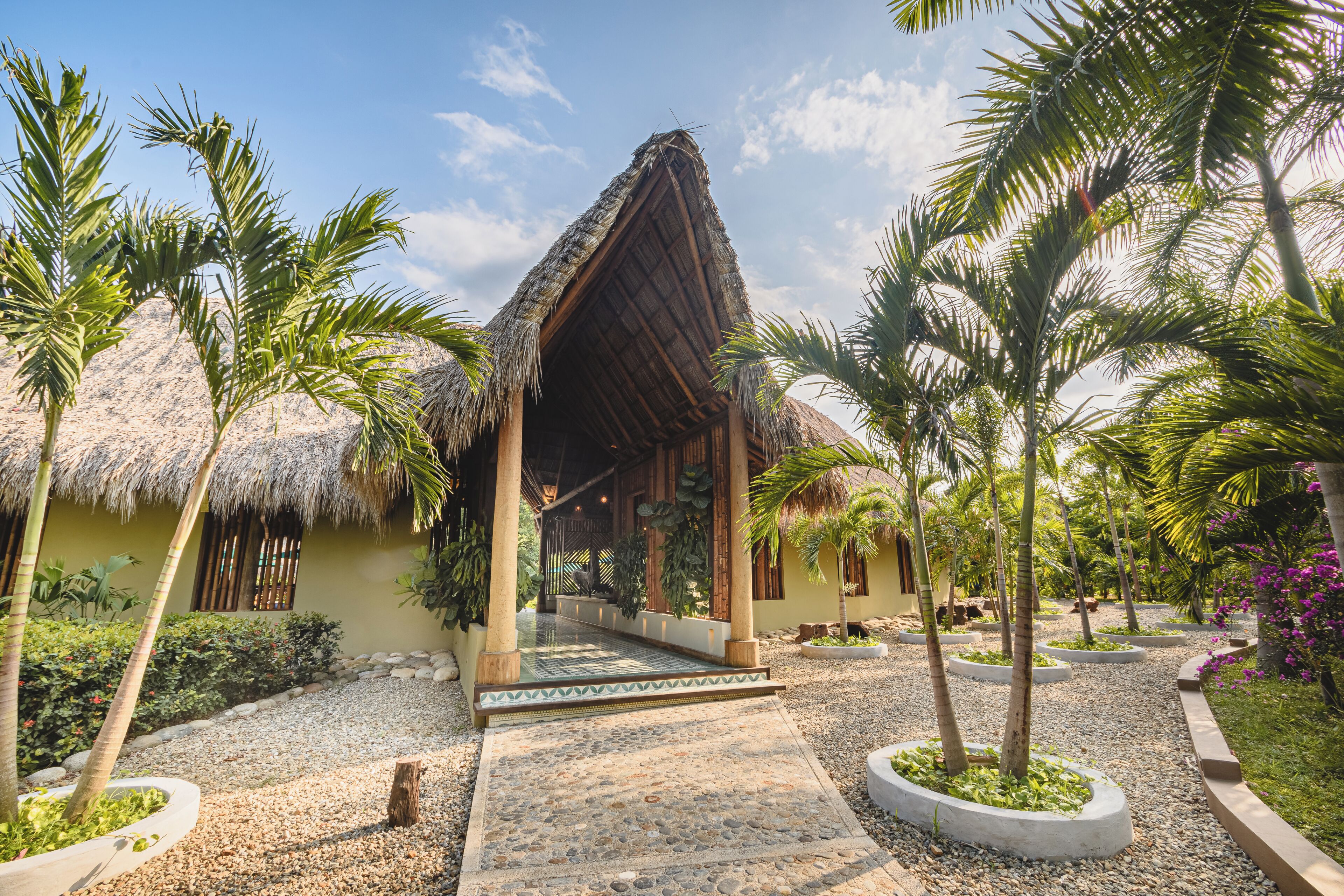 Un resort con una estructura de techo de paja, palmeras y un camino de grava.