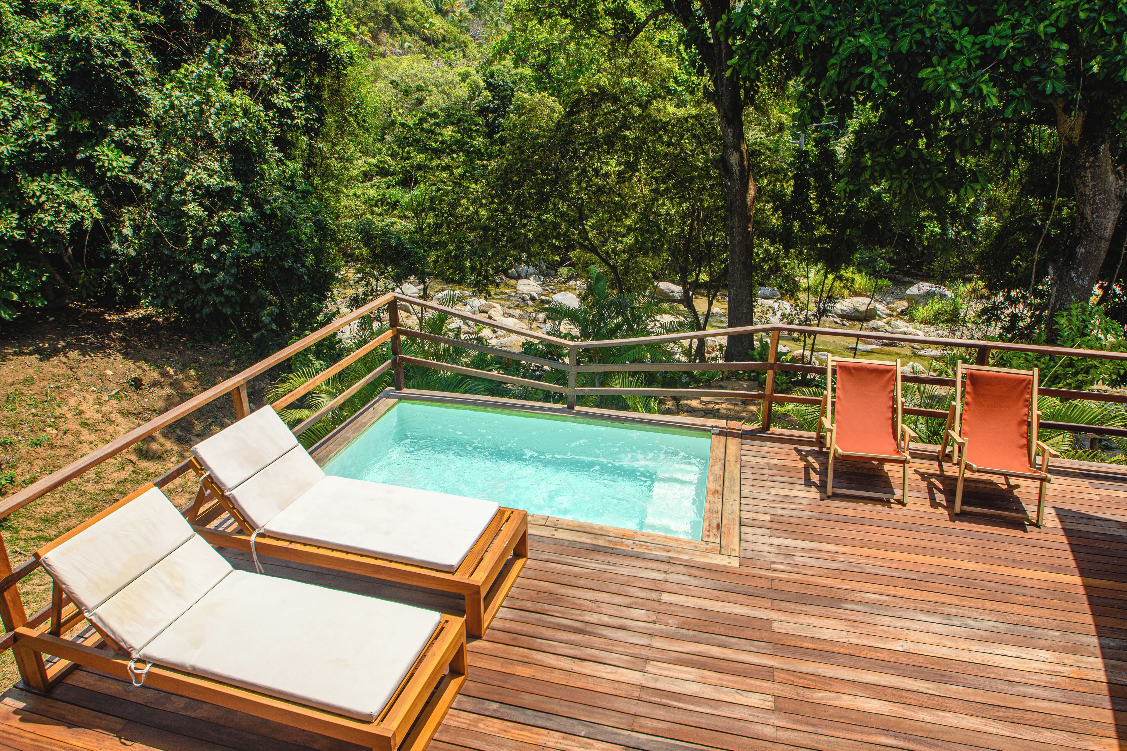 Una terraza de madera con piscina, sillas de descanso y vistas a un paisaje natural.
