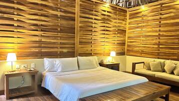 A room with a wooden slatted wall, a bed with white bedding, a wooden bench, and a sofa with cushions.