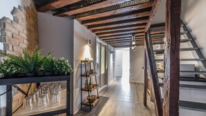 A hallway with exposed wooden beams, a brick wall, and a staircase. There are potted plants and a shelf with glasses and bottles. - PLAZA MAYOR by MONARO***** (Madrid)